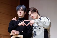 two young men standing next to each other making a heart shape with their hands while holding a teddy bear