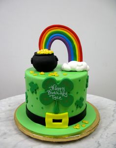 a green cake with a rainbow and pot of gold on top, sitting on a table