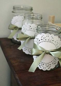 four mason jars with lace doily and green bows on them sitting on a table