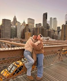 two people standing on top of a bridge with their arms around each other and the city in the background