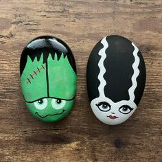 two painted rocks sitting on top of a wooden table next to each other with faces