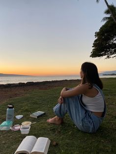 a woman sitting on the grass next to an open book and water bottle at sunset