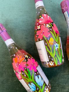 three wine bottles with flowers painted on them are sitting next to each other and one is empty