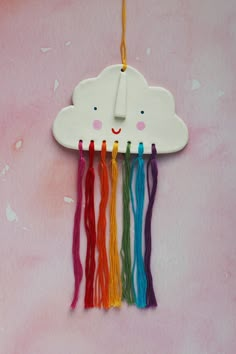 a white cloud hanging from a string on a pink background with multicolored thread