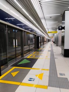 an empty subway station with yellow and green arrows painted on the floor next to doors