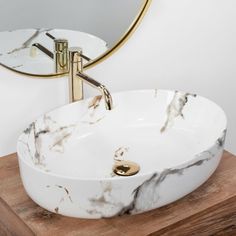 a marble sink with gold faucet and round mirror above it on a wooden stand