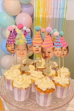 there are cupcakes with faces on them sitting on a cake plate in front of balloons and streamers