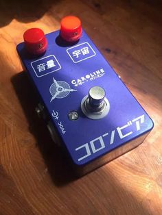 a purple guitar pedal sitting on top of a wooden table next to two red knobs