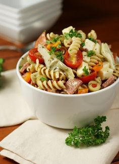 a white bowl filled with pasta salad on top of a wooden table