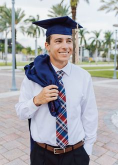 a man wearing a blue graduation cap and tie with his hands in his pockets smiling