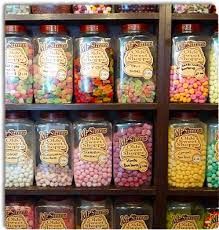 many jars filled with different types of candies on display in front of a wooden shelf