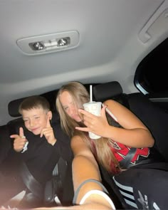 two children sitting in the back seat of a car with their cell phones up to their ears