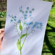 a person holding up a piece of paper with blue flowers on it