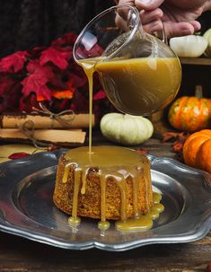 someone pouring caramel sauce over a cake on a plate with pumpkins in the background