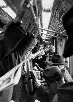 black and white photo of people sitting on a bus with hats hanging from the ceiling