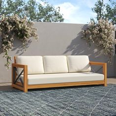 a wooden couch sitting on top of a blue rug next to a wall with white flowers