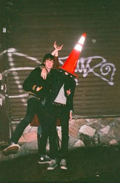 two young men standing next to each other in front of a wall with graffiti on it