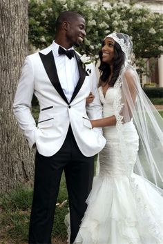 a bride and groom standing next to each other in front of a tree wearing tuxedos