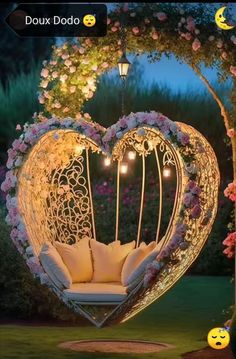 a heart shaped swing chair in the middle of a garden with flowers and lights hanging from it