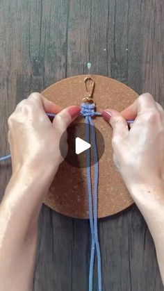 two hands are working on a piece of cork with blue string and a wooden circle