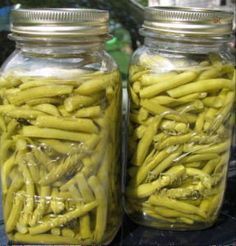 two jars filled with green beans sitting on top of a table next to each other