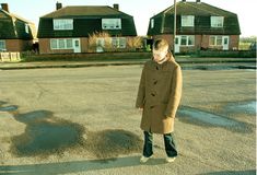 a woman standing in the middle of an empty parking lot with houses in the background