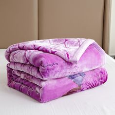 a stack of purple blankets sitting on top of a bed