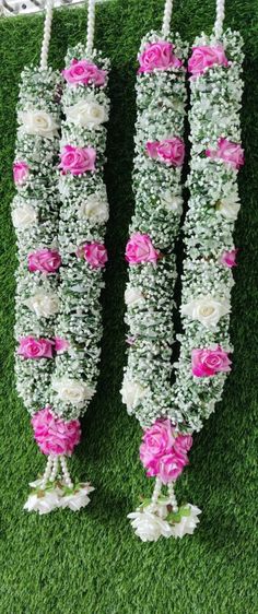 three flowers are hanging from the grass with string attached to each flower arrangement, which is decorated with white and pink flowers