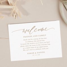 a welcome card sitting on top of a table next to some dried flowers and leaves