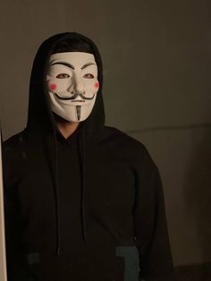 a person with a mask on standing next to a wall in a dark room wearing a black hoodie