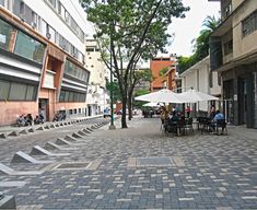 people are sitting at tables under umbrellas on the sidewalk in front of buildings and trees