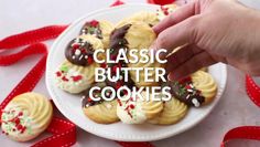 a hand picking up some cookies from a plate with red ribbon on the table next to it