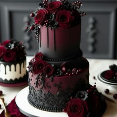 three tiered black and red wedding cake with flowers on it's top, sitting on a table