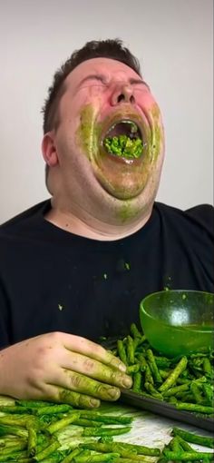 a man with green food on his face and hands in front of him eating asparagus