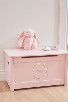 a pink toy chest sitting on top of a wooden floor next to a stuffed animal