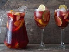 three pitchers and two glasses filled with liquid on top of a wooden table next to each other