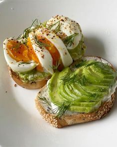 two pieces of bread with avocado and eggs on them sitting on a white plate