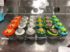 cupcakes decorated in different colors and designs on a tray with plastic dividers