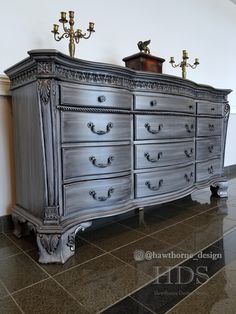 an antique dresser is painted silver and has two candle holders on top of the drawers