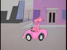 a pink car driving down a street next to tall buildings with flowers in the front