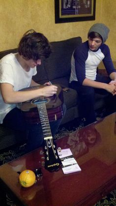 two young men sitting on a couch playing guitar