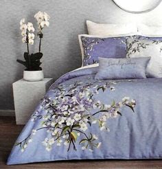 a bed with blue and white comforters in a room next to a vase filled with flowers