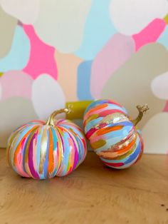 two colorful striped pumpkins sitting on top of a wooden table next to a wall