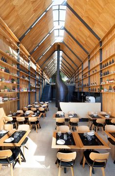 the inside of a restaurant with wooden tables and chairs in front of shelves filled with bottles