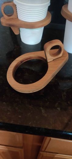 a wooden toilet seat on top of a black counter next to white plates and cups