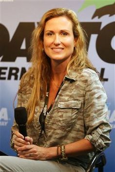 a woman sitting in a chair holding a microphone and smiling at the camera while wearing a camo shirt