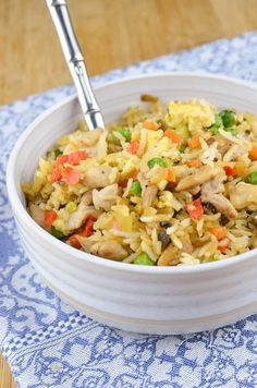 a bowl filled with rice and vegetables on top of a blue table cloth next to a fork