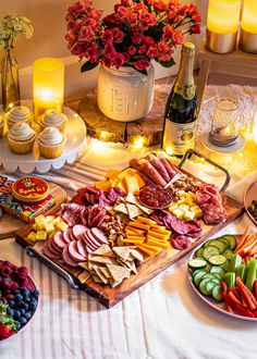 an assortment of food is displayed on a table with candles and flowers in the background