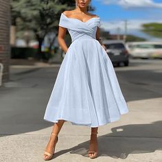 a woman in a blue dress is standing on the sidewalk and looking at the camera