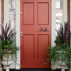 a red front door with two planters next to it and the word hello written in black